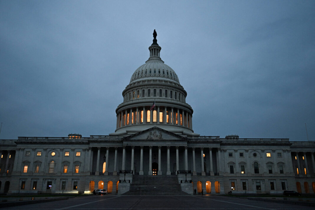 Capitólio dos Estados Unidos visto de frente ao anoitecer, com luzes internas acesas e céu nublado ao fundo.