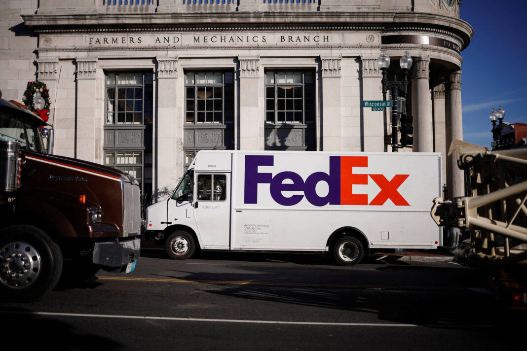 Caminhão de entrega FedEx branco está estacionado em frente ao prédio com fachada clássica onde se lê 