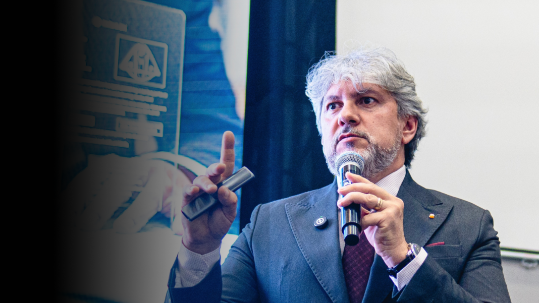 Luciano Menezes durante palestra, segurando microfone e fazendo gesto técnico, em ambiente corporativo, abordando estratégia fiscal e gestão empresarial.