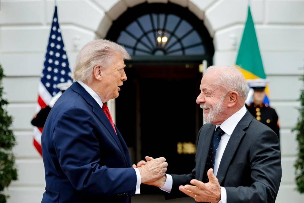 Dois homens de terno, um com gravata vermelha e outro com gravata azul, apertam as mãos e sorriem em frente à entrada da Casa Branca. Bandeiras dos Estados Unidos e do Brasil estão visíveis ao fundo.