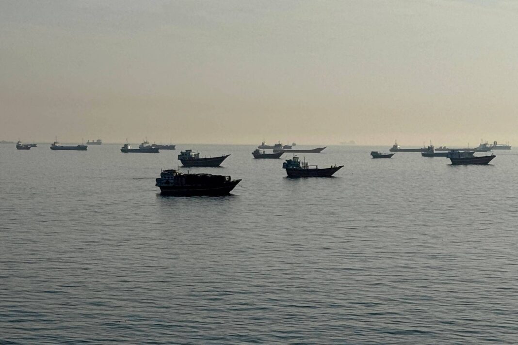 Diversos barcos flutuam sobre águas calmas em mar aberto sob céu claro e neblina leve no horizonte.