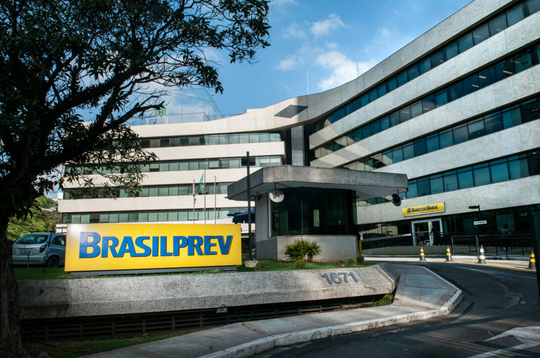 Prédio moderno de escritórios com fachada curva e janelas horizontais azuis. Placa amarela com texto azul 